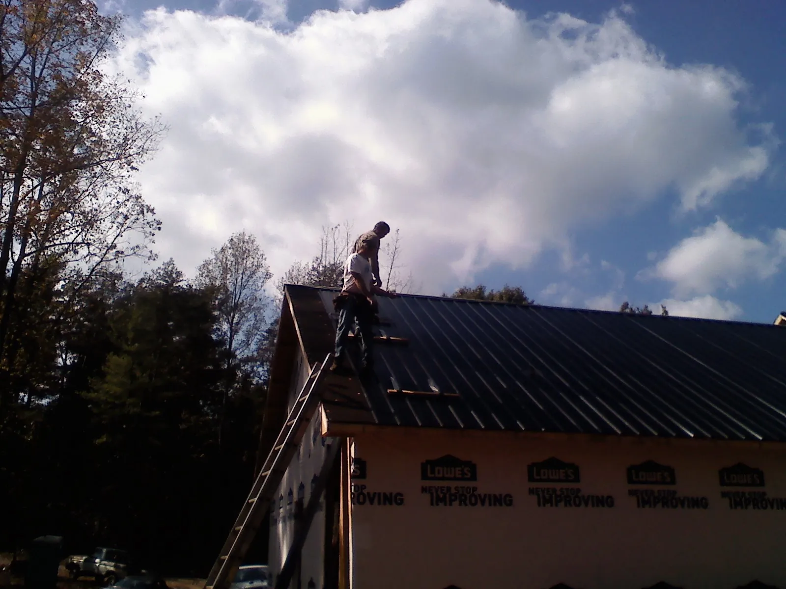 Roofer fastening dark metal panels high against a cloudy sky, from a Roof Inspection job in Roscoe